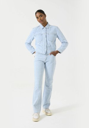 Lichtblauwe denimjack en bijpassende broek met een gestructureerd patroon. De outfit heeft een klassieke kraag en voorzakken.