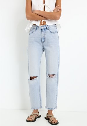 Lichtblauwe, hoog-waist jeans met versleten knieën. Met een rechte pasvorm en rafelige zoom. Gepaard met beige sandaaltjes met bandjes.