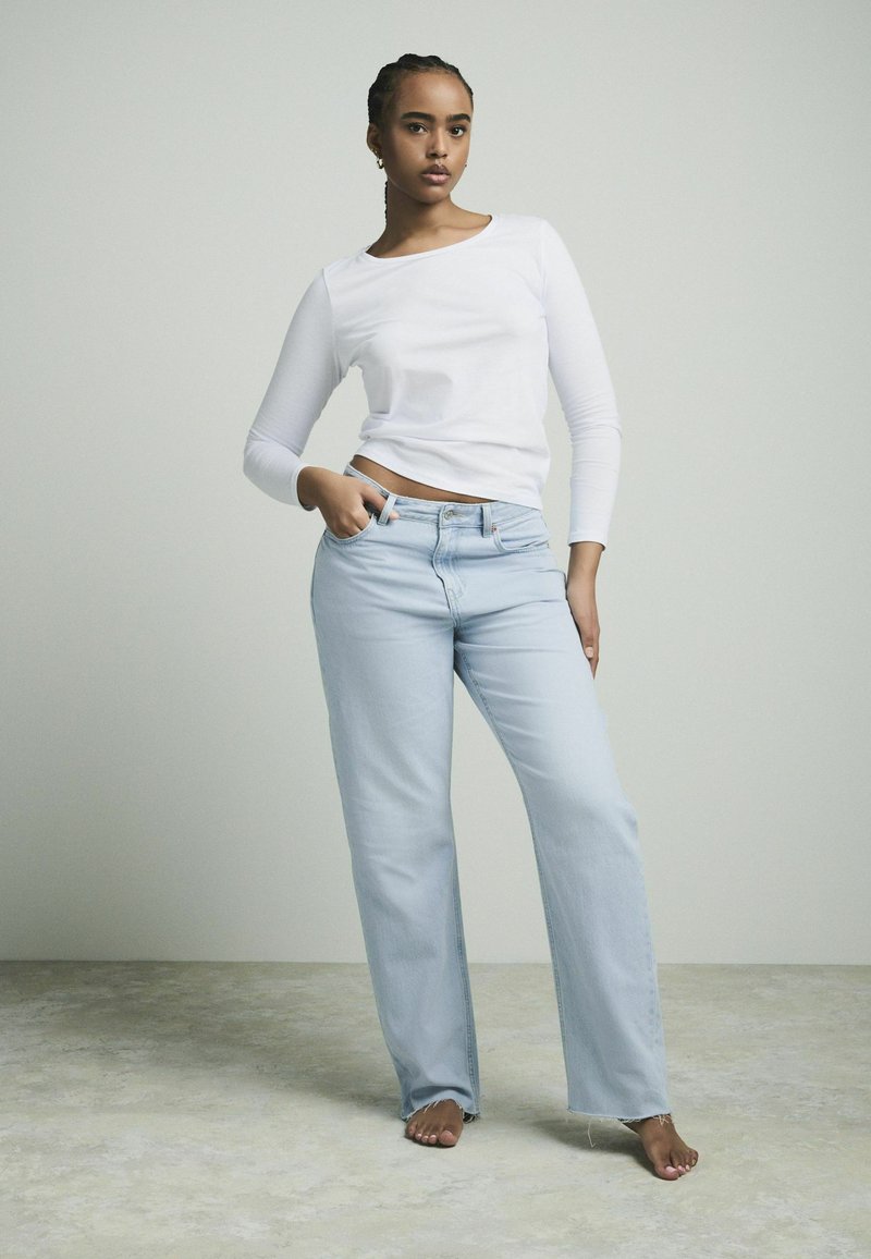 Lichtgewassen denim jeans met een relaxte pasvorm, gecombineerd met een witte lange mouwen top. Zichtbare stiksels en lichte rafeling aan de onderkant.