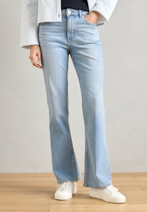 Lichtblauwe flare jeans van denim, met een hoge taille, subtiele vervaging en een nette afwerking aan de pijpen. Gepaard met witte sneakers.