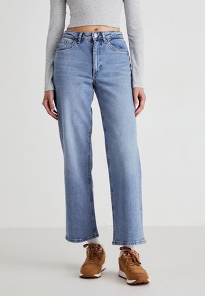 Lichtblauwe wijde jeans met een hoge taille, voorzien van twee zijzakken en een ritssluiting. Draagt met bruine sneakers en een grijze langemouwen top.