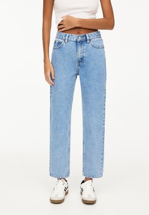 Lichtblauwe hoge taille jeans met een rechte pijp, voorzien van frontzakken en een knoopsluiting, gedragen met witte sneakers.