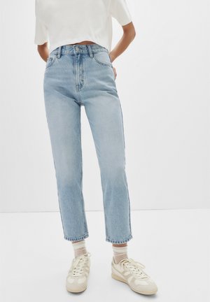 Lichtblauwe high-waisted jeans met een recht uiteinde ontwerp, voorzien van een klassieke knoopsluiting en subtiele vervaging, gecombineerd met beige sneakers.