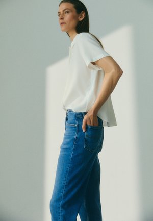 Witte korte mouwen shirt gemaakt van zachte stof; blauwe high-waisted jeans met een klassiek snit en details van de achterzak; minimalistisch ontwerp.